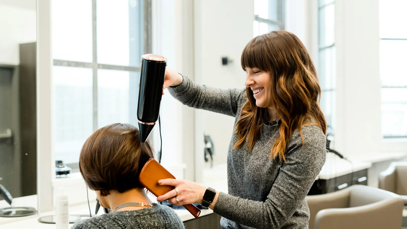 Friseurin föhnt einer Kundin die Haare im hellen Salon